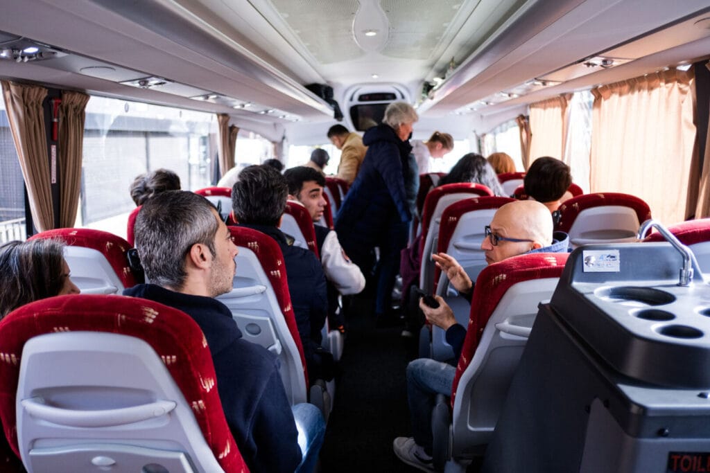 A group of people are sat down on a coach. They are talking to each other across the asile.