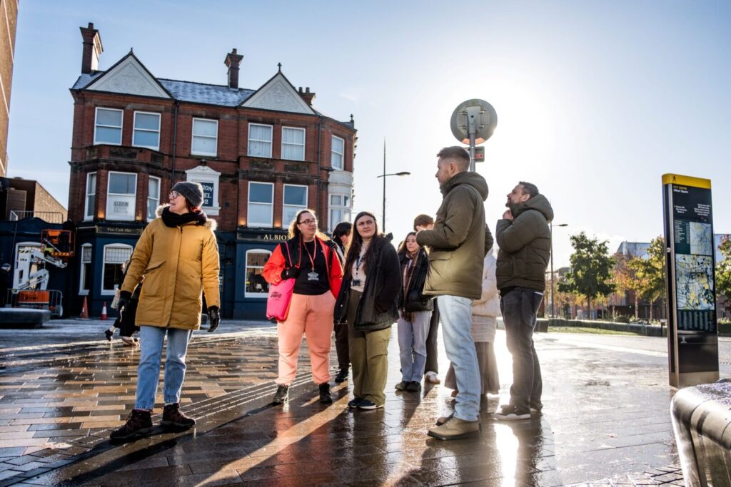 A group of young people are standing in an open, paved area with a pub behind them called The Albion.