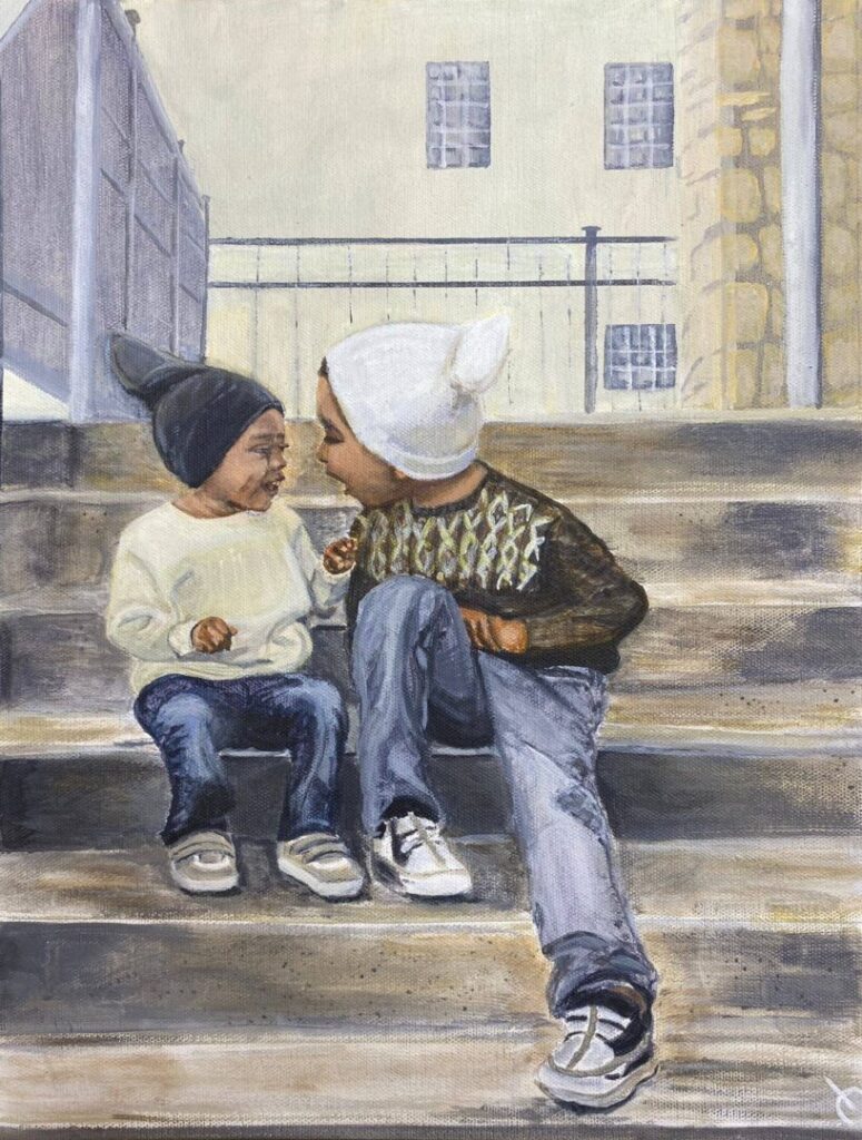 Two children sit on outdoor steps, dressed warmly in jumpers, jeans and hats. They are happily leaning into one another, laughing. The background features buildings and railings.