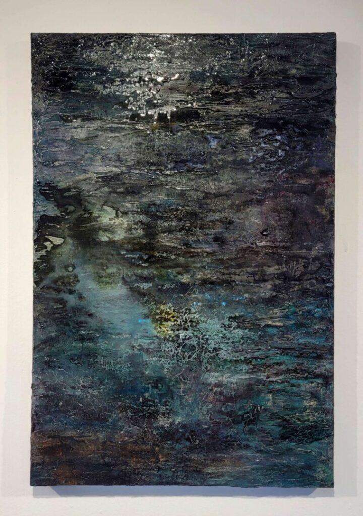 An abstract artwork with a rich, layered texture and a dark palette of black, blue, and green. Lighter tones of white and yellow emerge from the depths.