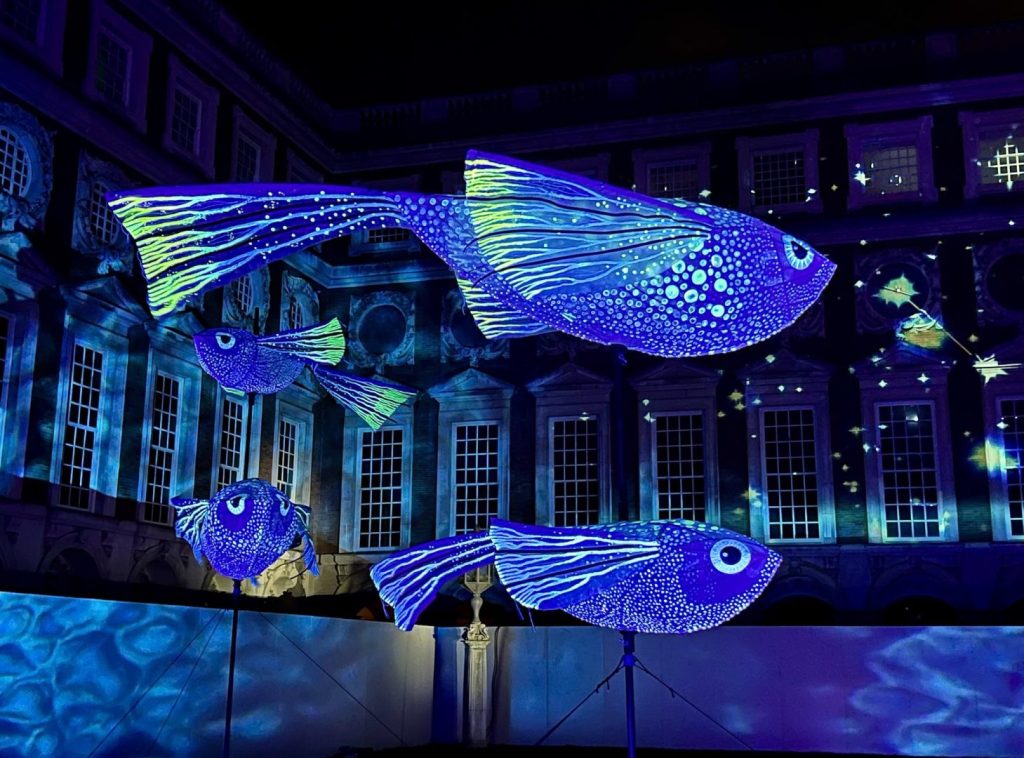 Glowing fish sculptures stand high on poles against a dark backdrop.