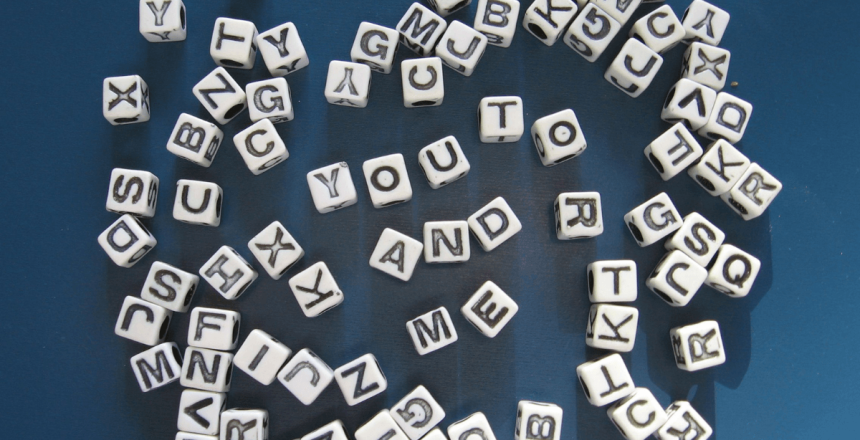 Lots of small, cubed white beads are scattered across a blue background. The beads all have letters on. There are eight in the centre that are laid out to read 'You and Me'.